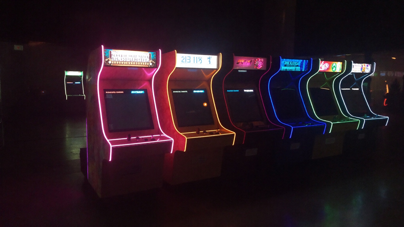 Dim arcade room lined with glowing retro cabinets casting magenta and cyan light across the floor